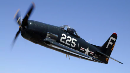 Grumman F8F Bearcat military aircraft (tail 225) banking in flight with spinning propeller against a clear blue sky — HD PC desktop wallpaper/background.