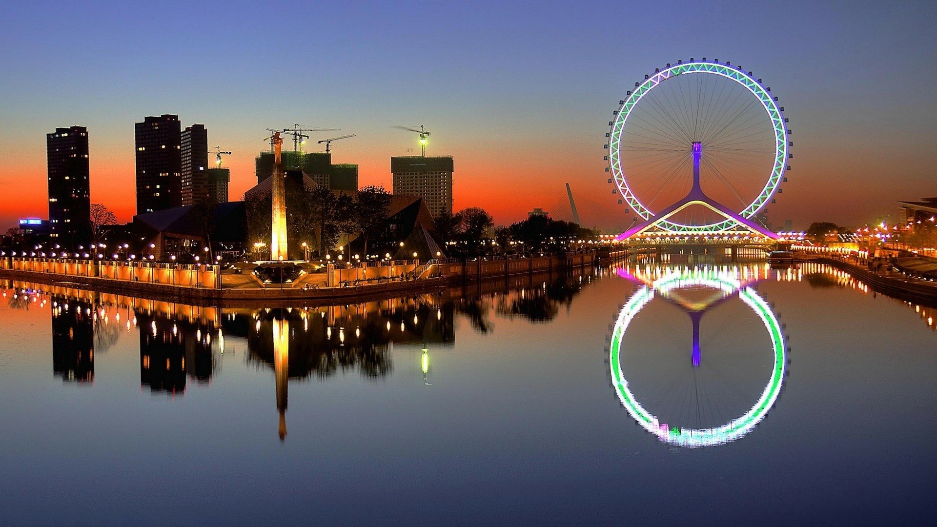 HD desktop wallpaper of Tianjin, China at sunset featuring illuminated cityscape and the Tianjin Eye Ferris wheel reflected on calm waters.