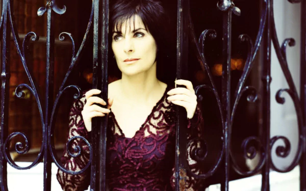 HD music desktop wallpaper: contemplative female singer behind ornate wrought-iron bars, wearing deep plum lace, moody Enya-inspired atmosphere.