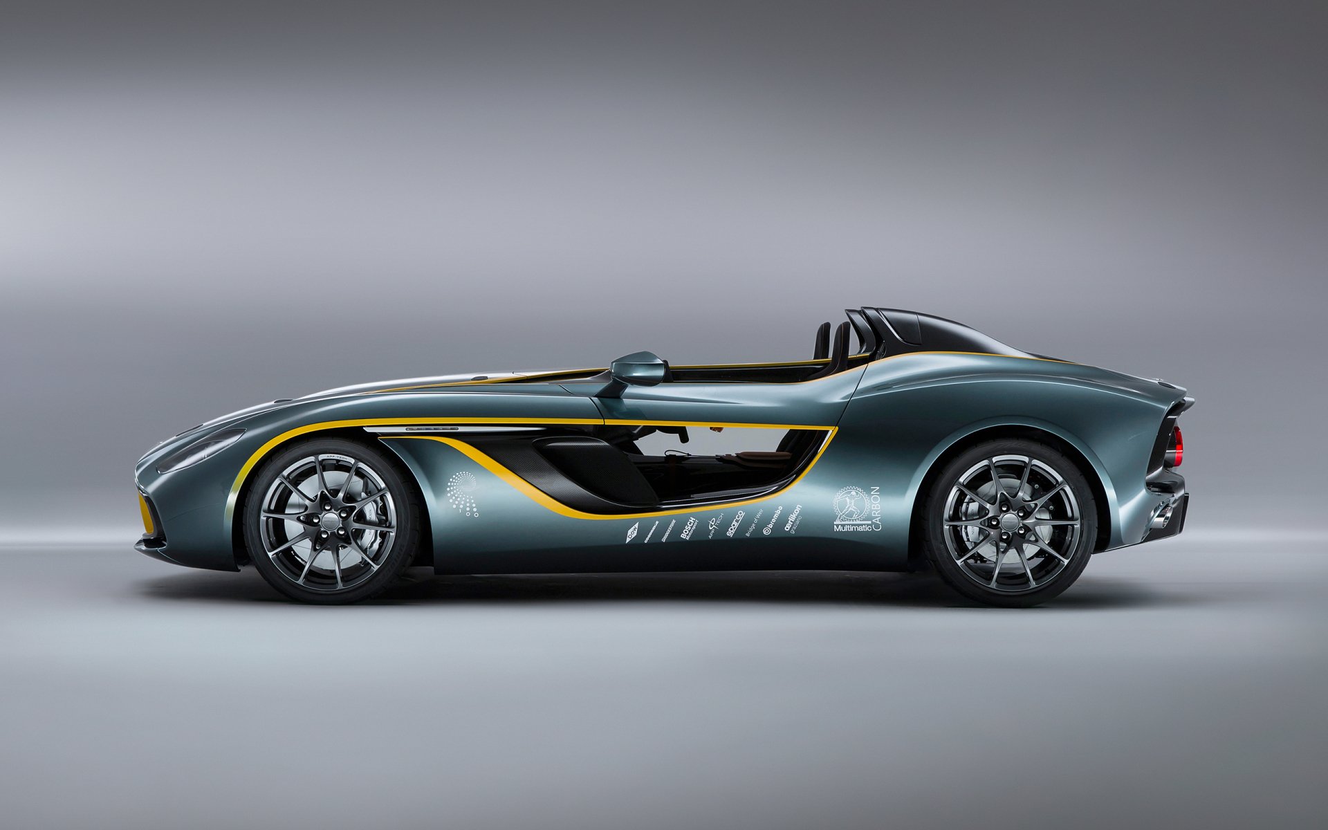 Aston Martin CC100 roadster side profile — metallic gray vehicle with yellow accents, rendered as a 2K Quad HD PC desktop wallpaper background.