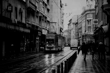 Black and white HD cityscape of a man-made urban street in Sofia, Bulgaria, featuring trams, historic buildings, and pedestrians on a wet pavement.