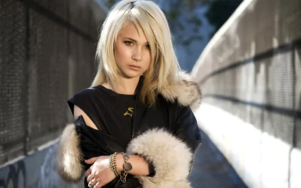 HD desktop wallpaper featuring celebrity Juno Temple standing outdoors wearing a black coat with fur trim, against a blurred urban background.