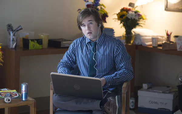 HD wallpaper from Alpha House featuring a person at a desk with a laptop, surrounded by clutter, suitable as a desktop background.