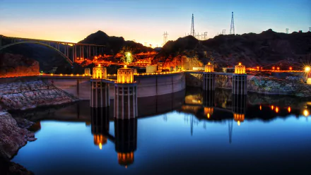4K Ultra HD image of the man-made Hoover Dam at dusk, showcasing illuminated structures and calm water reflecting the dam and surrounding hills.