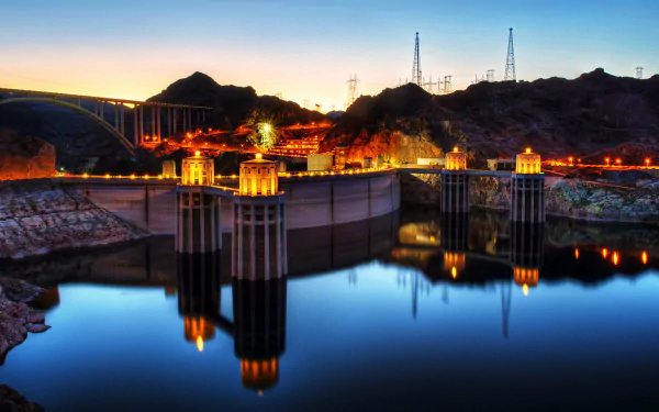 4K Ultra HD image of the man-made Hoover Dam at dusk, showcasing illuminated structures and calm water reflecting the dam and surrounding hills.