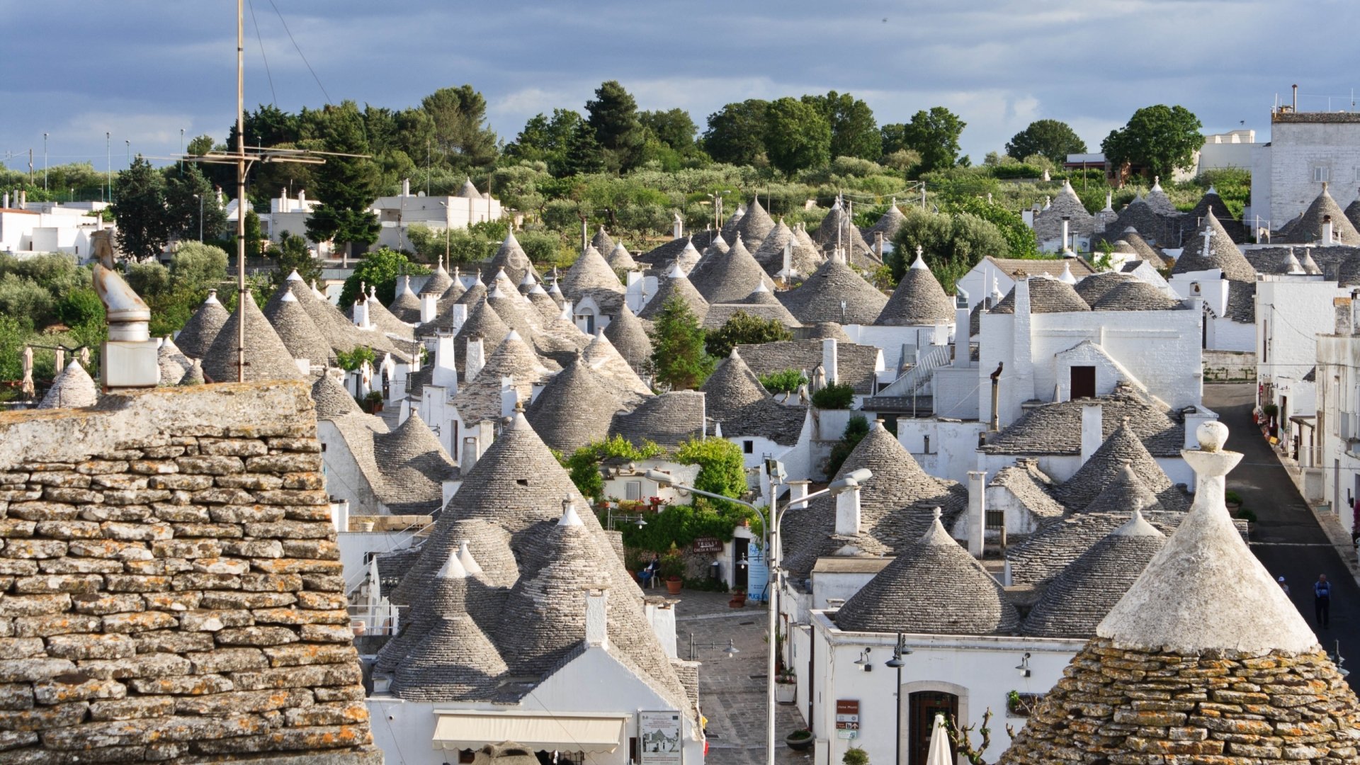 Man-made trulli village in Alberobello, Italy, whitewashed houses with conical stone roofs beneath a blue sky — 2K Quad HD PC desktop wallpaper/background.