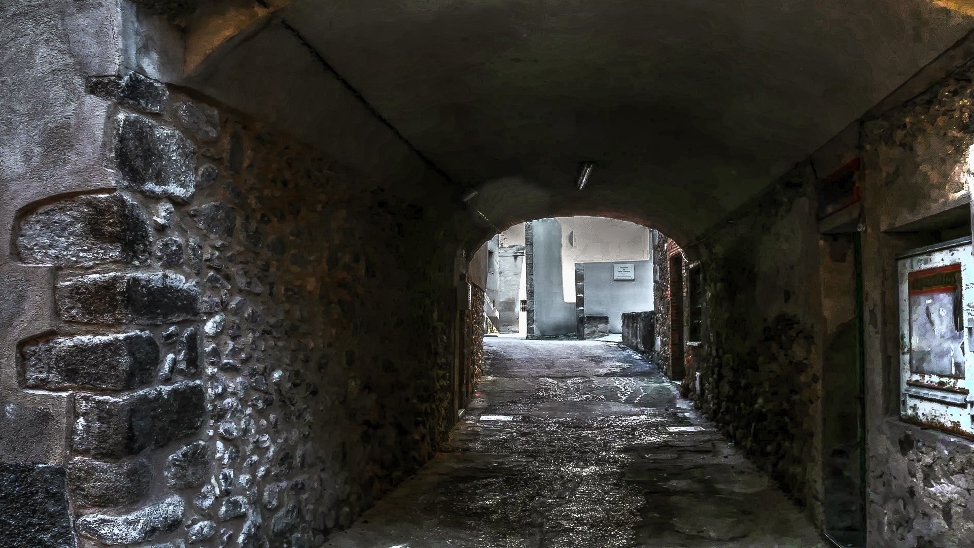 HD desktop wallpaper of a dimly lit, narrow man-made alleyway with stone walls and an arched ceiling leading to a brighter street beyond.
