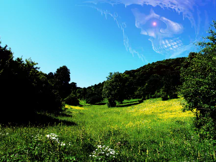 Dark artistic 2K Quad HD PC desktop wallpaper and background: sunlit green meadow and tree-lined hills beneath a vivid blue sky with a faint ghostly skull forming in the clouds.