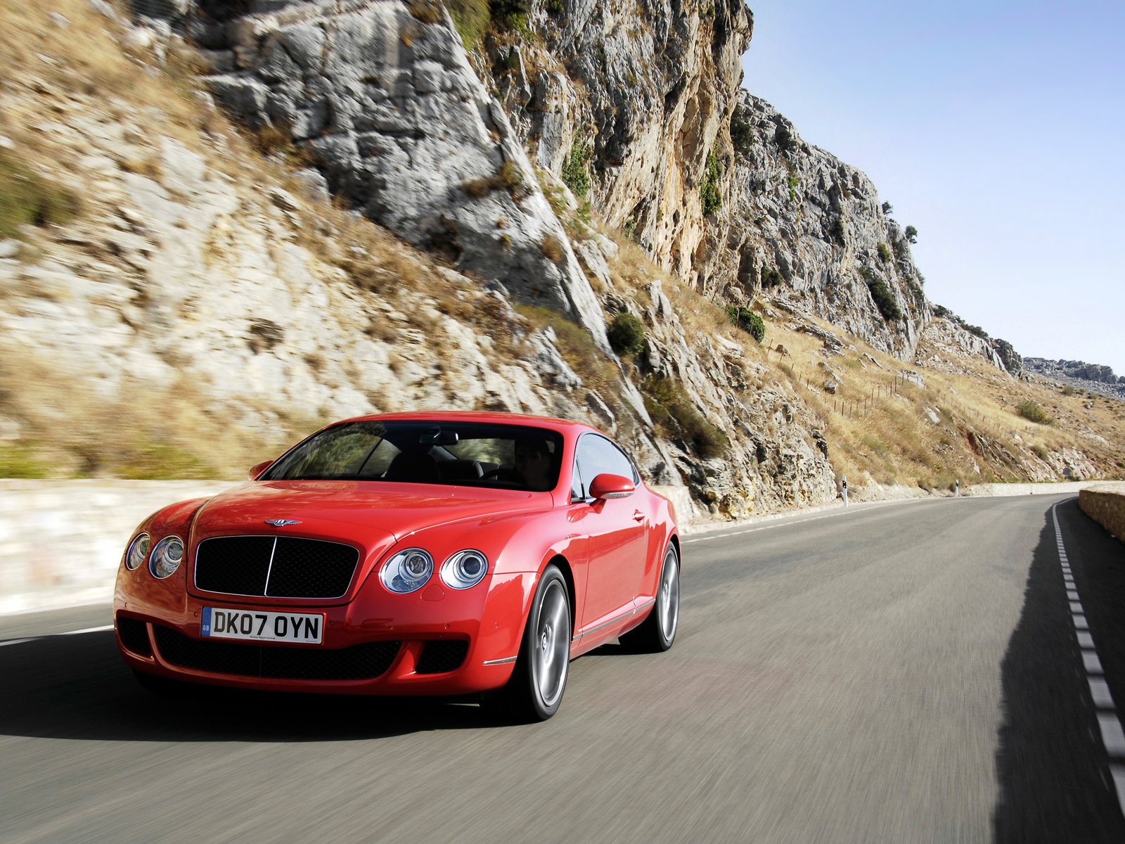 Red Bentley Continental GT Speed driving on a winding mountain road, captured in a high-definition desktop wallpaper.
