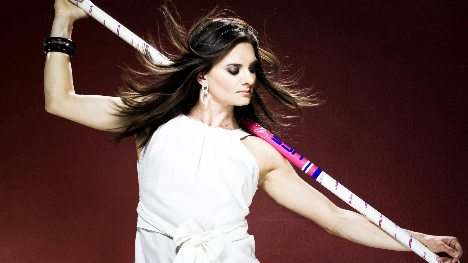 HD desktop wallpaper featuring Yelena Isinbayeva, poised with a pole vault pole, set against a deep red background showcasing her athletic grace in sports.