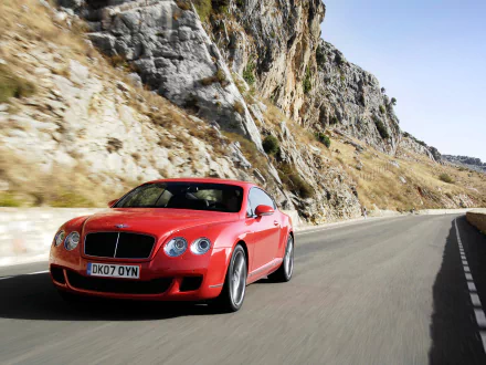 Red Bentley Continental GT Speed driving on a winding mountain road, captured in a high-definition desktop wallpaper.