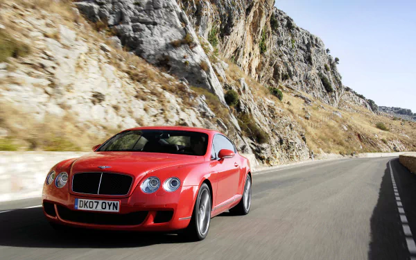 Red Bentley Continental GT Speed driving on a winding mountain road, captured in a high-definition desktop wallpaper.