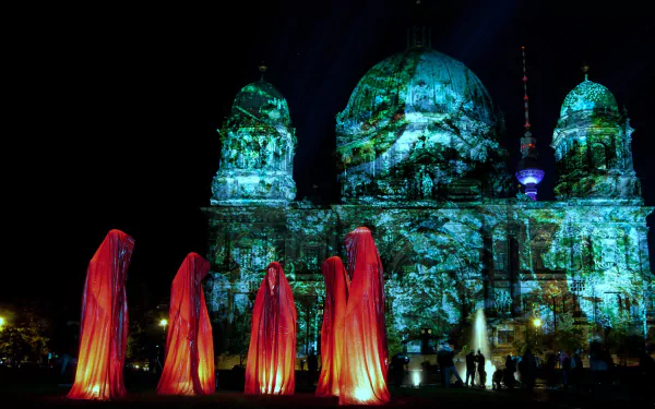 Artistic Festival of Lights - Berlin wallpaper: Berlin Cathedral bathed in green-blue projections with four red-lit cloaked figures in the foreground. HD PC desktop wallpaper/background.