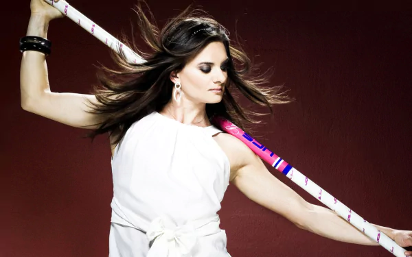 HD desktop wallpaper featuring Yelena Isinbayeva, poised with a pole vault pole, set against a deep red background showcasing her athletic grace in sports.