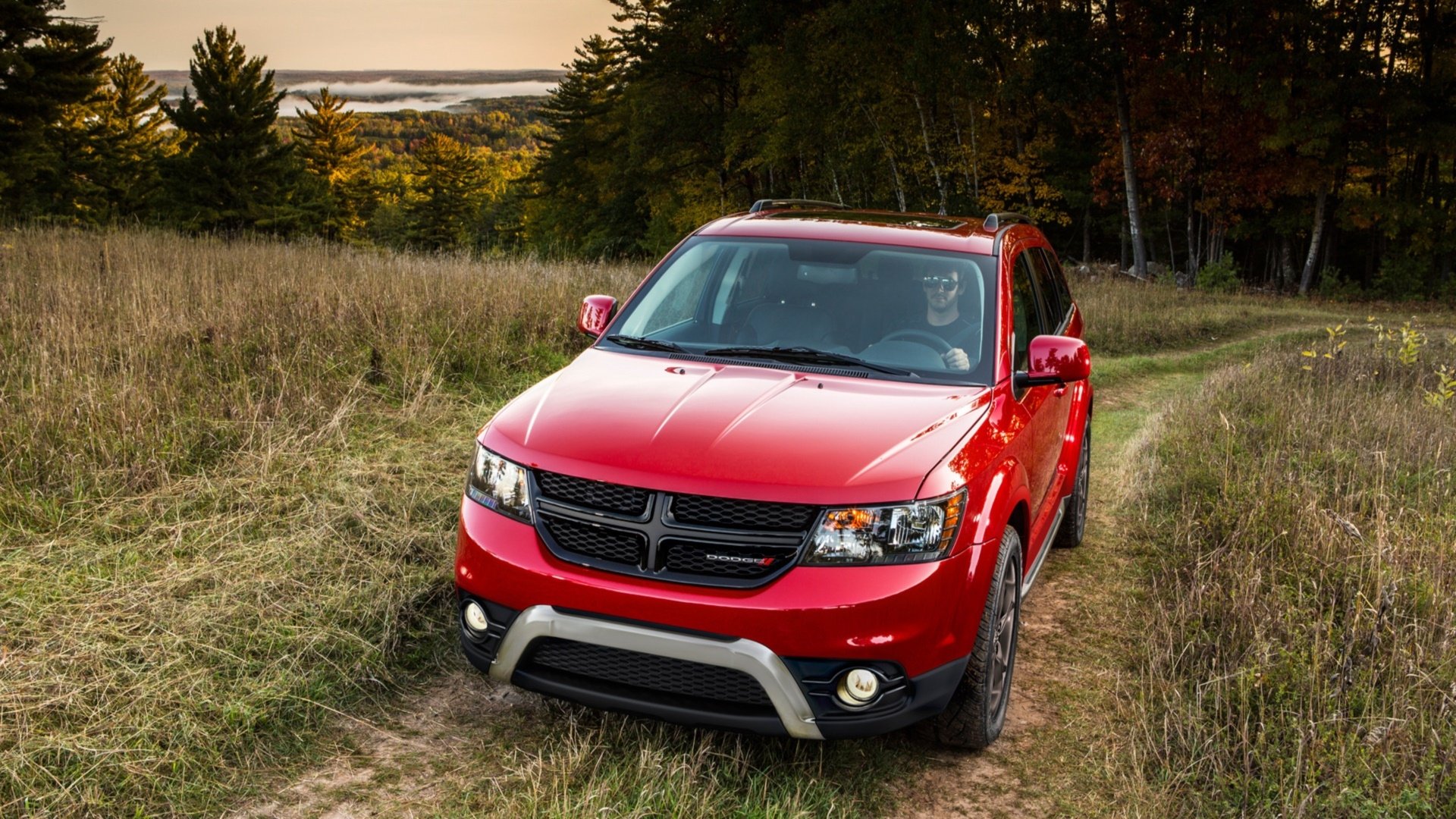 Red Dodge Journey parked on a grassy trail surrounded by trees under a clear sky, captured in a high-definition PC desktop wallpaper and background.