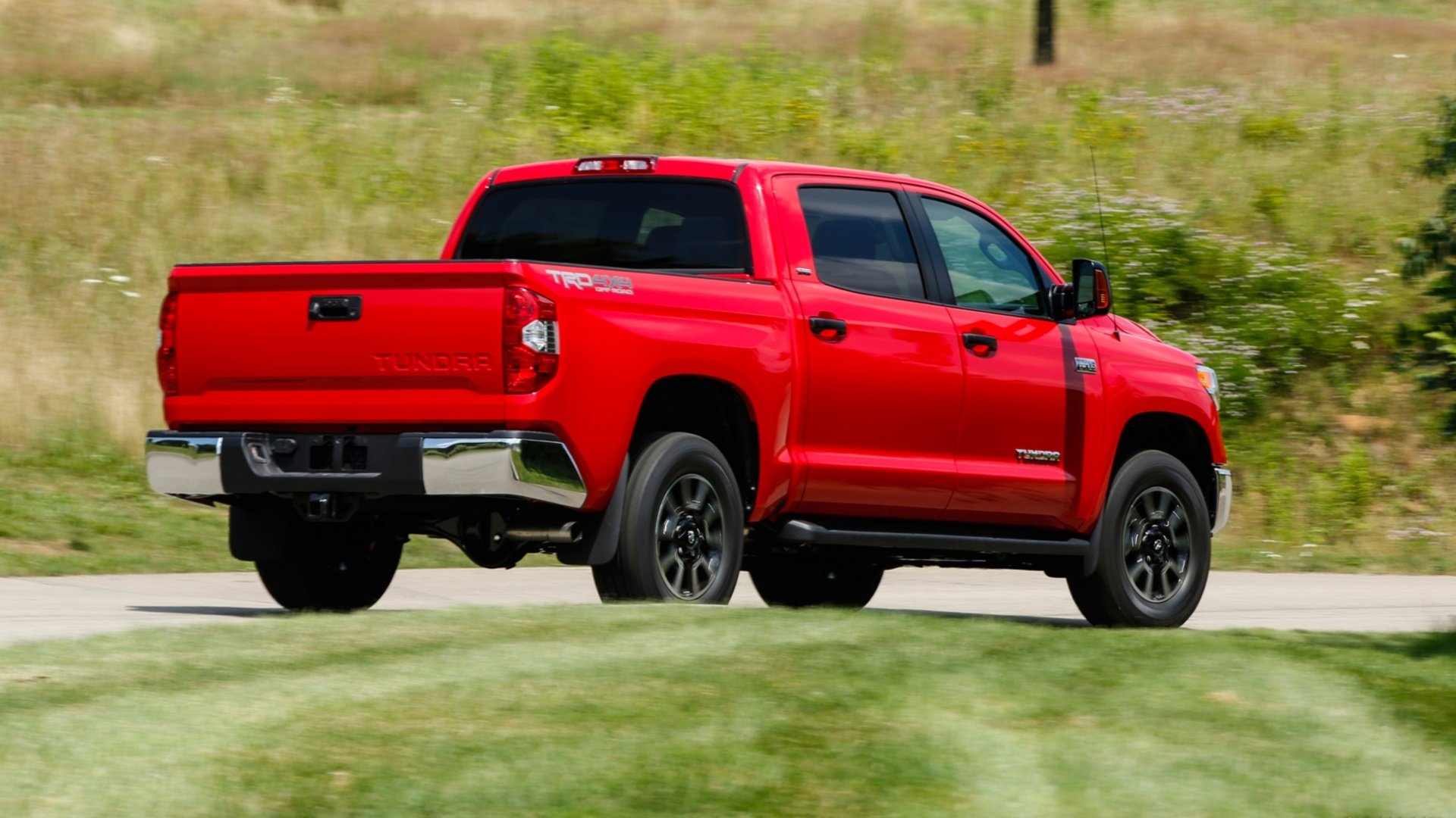 HD desktop wallpaper featuring a red Toyota Tundra truck driving on a road with grassy fields in the background.