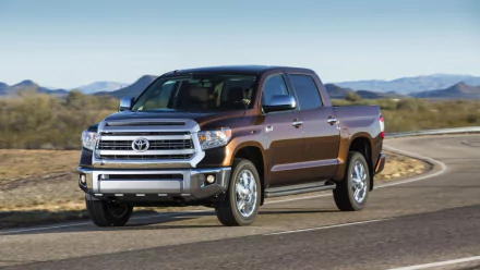 HD PC desktop wallpaper showing a brown Toyota Tundra pickup truck driving on a winding desert road with distant mountains.