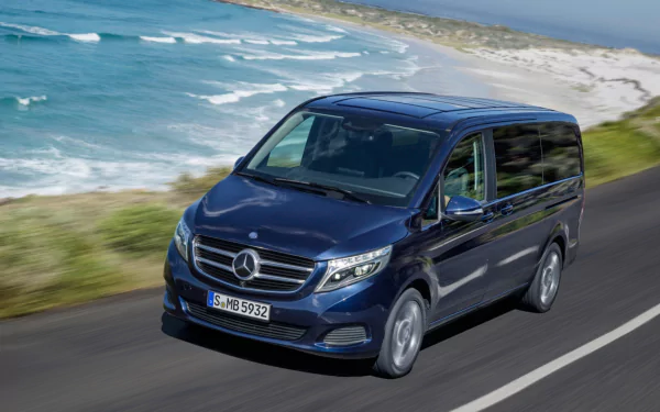 HD PC desktop wallpaper featuring a dark blue Mercedes-Benz V-Class driving along a coastal road by the ocean.