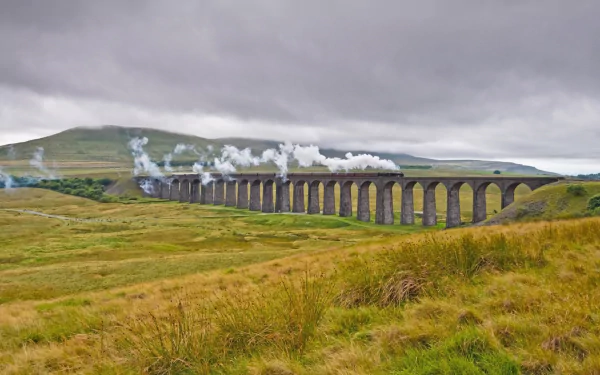 HD desktop wallpaper featuring a steam train crossing a long stone viaduct over green rolling hills under a cloudy sky.