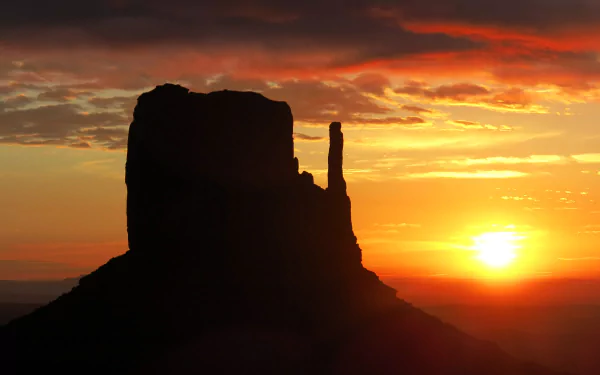 4K Ultra HD wallpaper of Monument Valley at sunset, showcasing the iconic rock formations silhouetted against a vibrant orange and yellow sky.