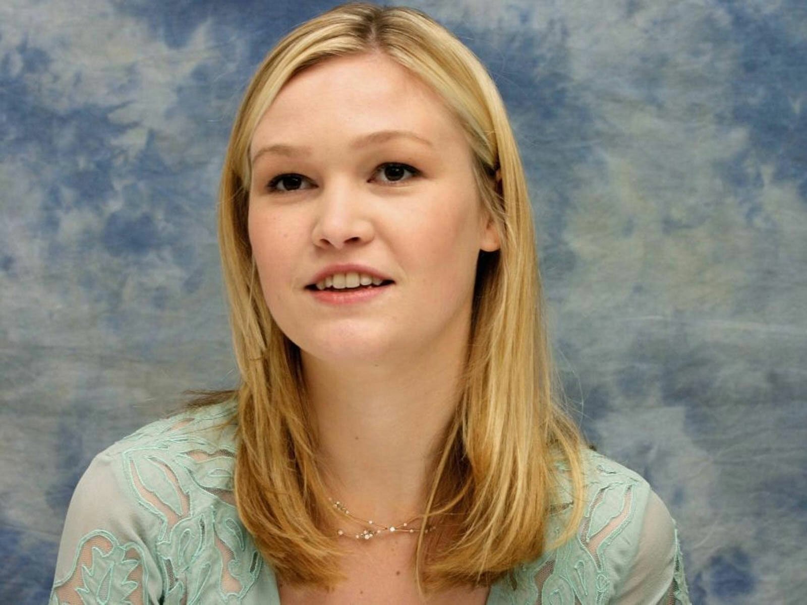A close-up of celebrity Julia Stiles, showcasing her blonde hair and soft smile against a blue textured background, captured in HD for a desktop wallpaper.