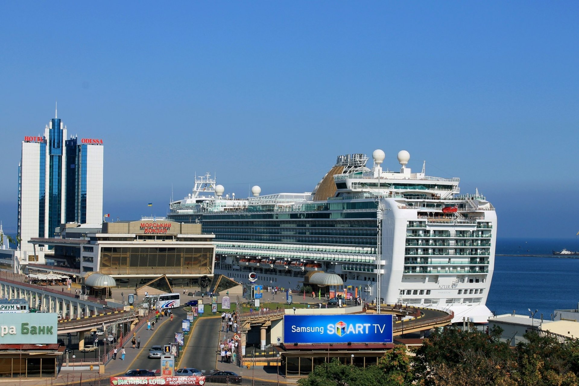 Man-made structures in Odessa featuring a large cruise ship docked at a busy port with modern buildings under a clear blue sky, captured in HD for a desktop wallpaper.