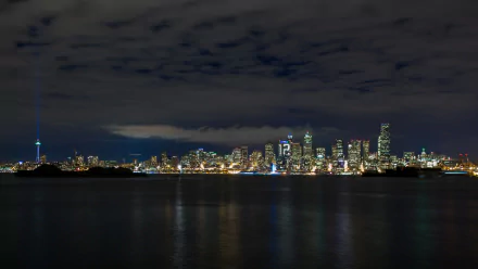 The image showcases a stunning view of Seattle's skyline at night, featuring the iconic Space Needle amidst a backdrop of illuminated buildings and a reflective water surface.