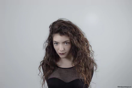 HD PC desktop wallpaper of a moody music singer with long curly dark hair and a mesh top against a soft gray background.