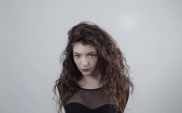 HD PC desktop wallpaper of a moody music singer with long curly dark hair and a mesh top against a soft gray background.