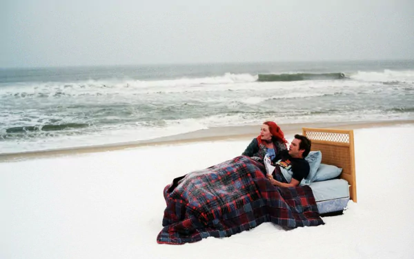 HD wallpaper from Eternal Sunshine of the Spotless Mind featuring two characters snuggled on a beach couch under a blanket.