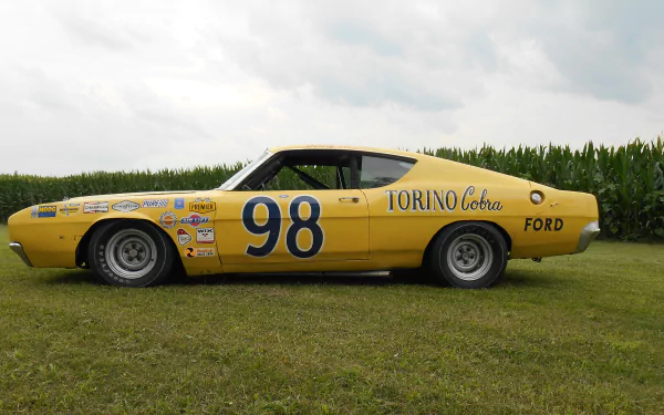 Yellow Ford Torino Cobra race car (#98) side view on grass beneath a cloudy sky — 5K Ultra HD PC desktop wallpaper and background.