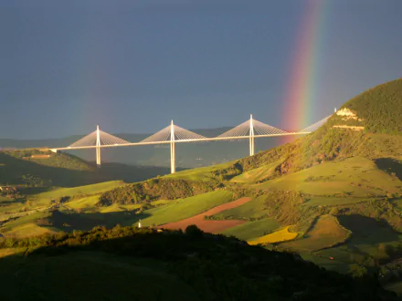 HD desktop wallpaper showcasing the Millau Viaduct, a stunning man-made bridge blending modern architecture with the natural landscape under a vibrant rainbow.
