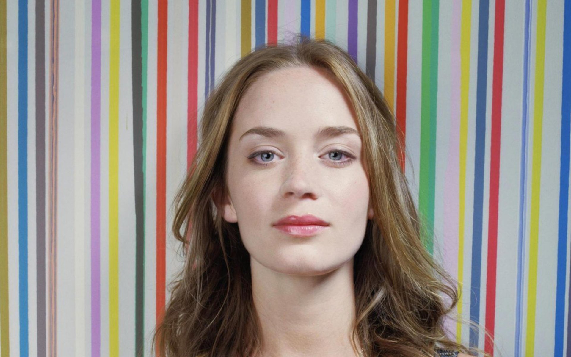 HD desktop wallpaper featuring English actress and celebrity Emily Blunt against a colorful striped background.