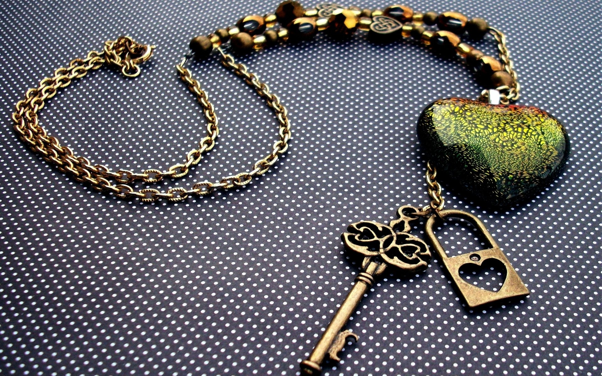 Man-made necklace with antique key, heart-shaped padlock and iridescent heart pendant on dotted fabric — HD PC desktop wallpaper and background.