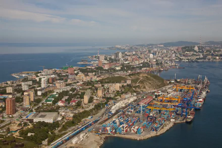 A 4K Ultra HD aerial view of Vladivostok's man-made port and cityscape along the coastline under a partly cloudy sky.