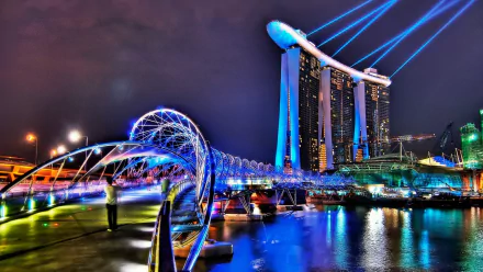 Night view of Singapore's Helix Bridge with vibrant lights and the illuminated Marina Bay Sands hotel in the background, captured as an HD desktop wallpaper.