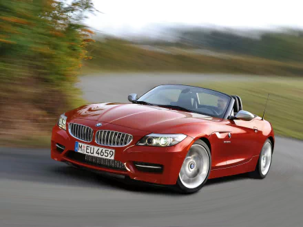 HD desktop wallpaper featuring a red BMW Z4 convertible driving on a curvy road with blurred greenery in the background.