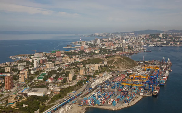 A 4K Ultra HD aerial view of Vladivostok's man-made port and cityscape along the coastline under a partly cloudy sky.