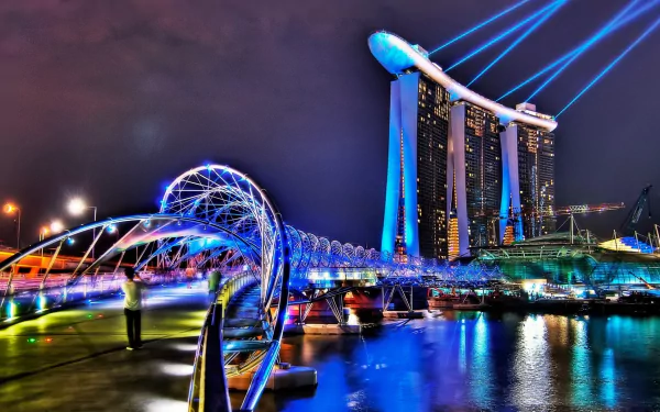Night view of Singapore's Helix Bridge with vibrant lights and the illuminated Marina Bay Sands hotel in the background, captured as an HD desktop wallpaper.