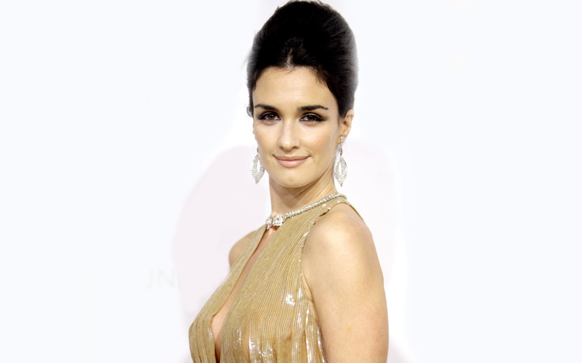 HD desktop wallpaper featuring Spanish actress and celebrity Paz Vega in an elegant gold dress against a white background.