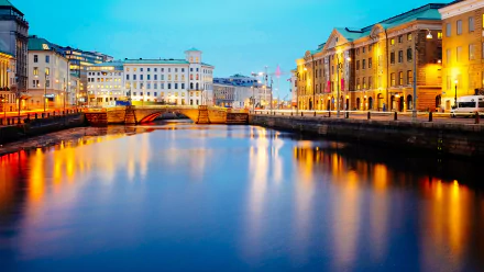A serene evening view of Gothenburg, showcasing illuminated buildings along the waterfront, with a bridge reflecting in the calm water below, captured in stunning 4K Ultra HD.
