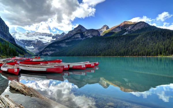 4K Ultra HD image of Lake Louise featuring red canoes floating on turquoise water, surrounded by forested mountains and a partly cloudy sky.