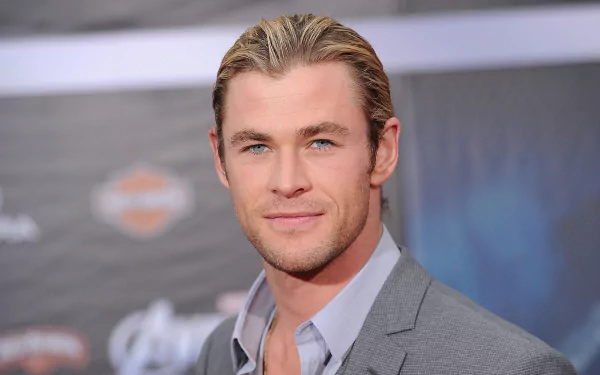 HD desktop wallpaper featuring Australian actor and celebrity Chris Hemsworth smiling in a gray suit with a blurred event backdrop.
