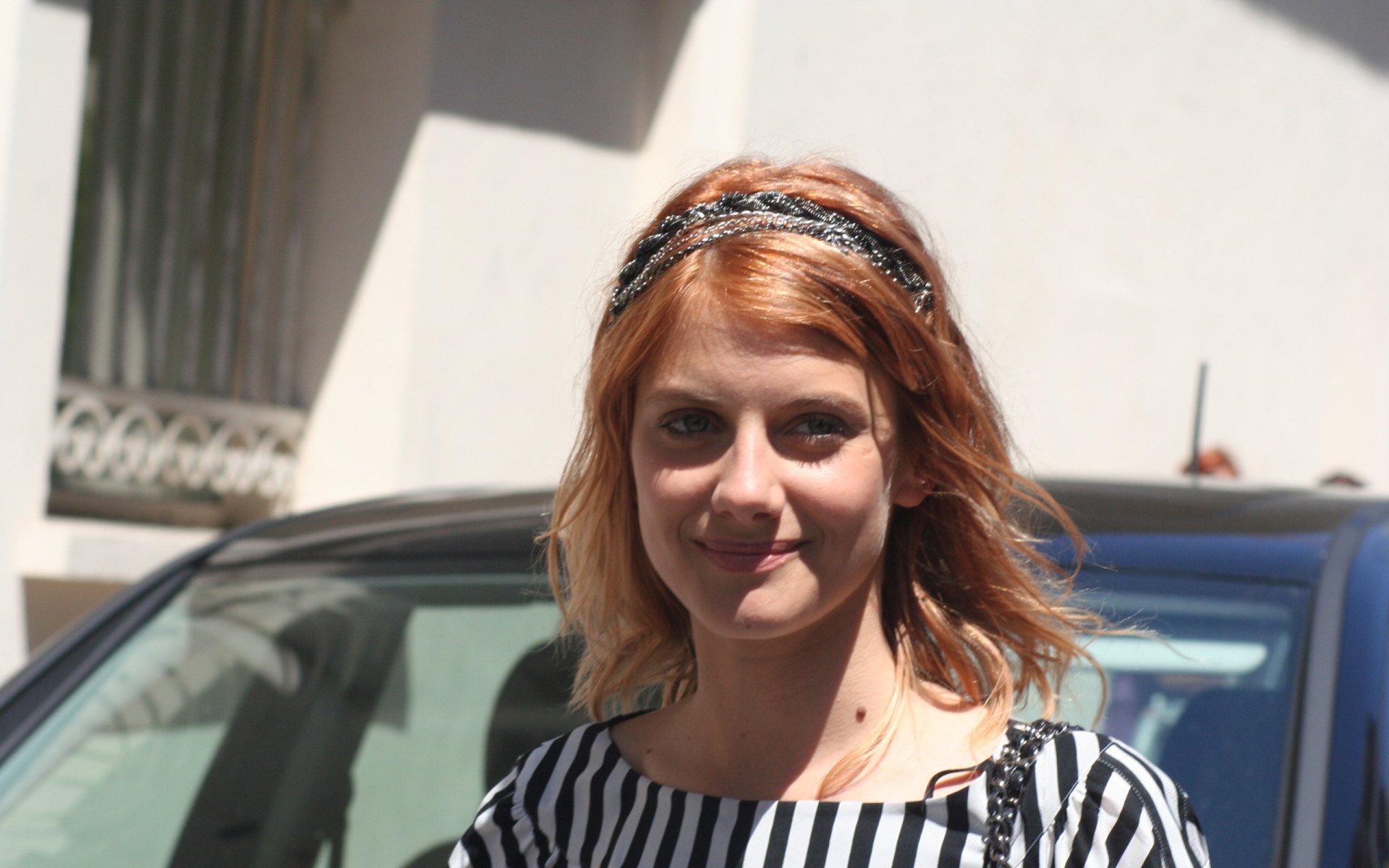 HD desktop wallpaper featuring French actress and celebrity Melanie Laurent outdoors with sunlight highlighting her red hair and striped top.