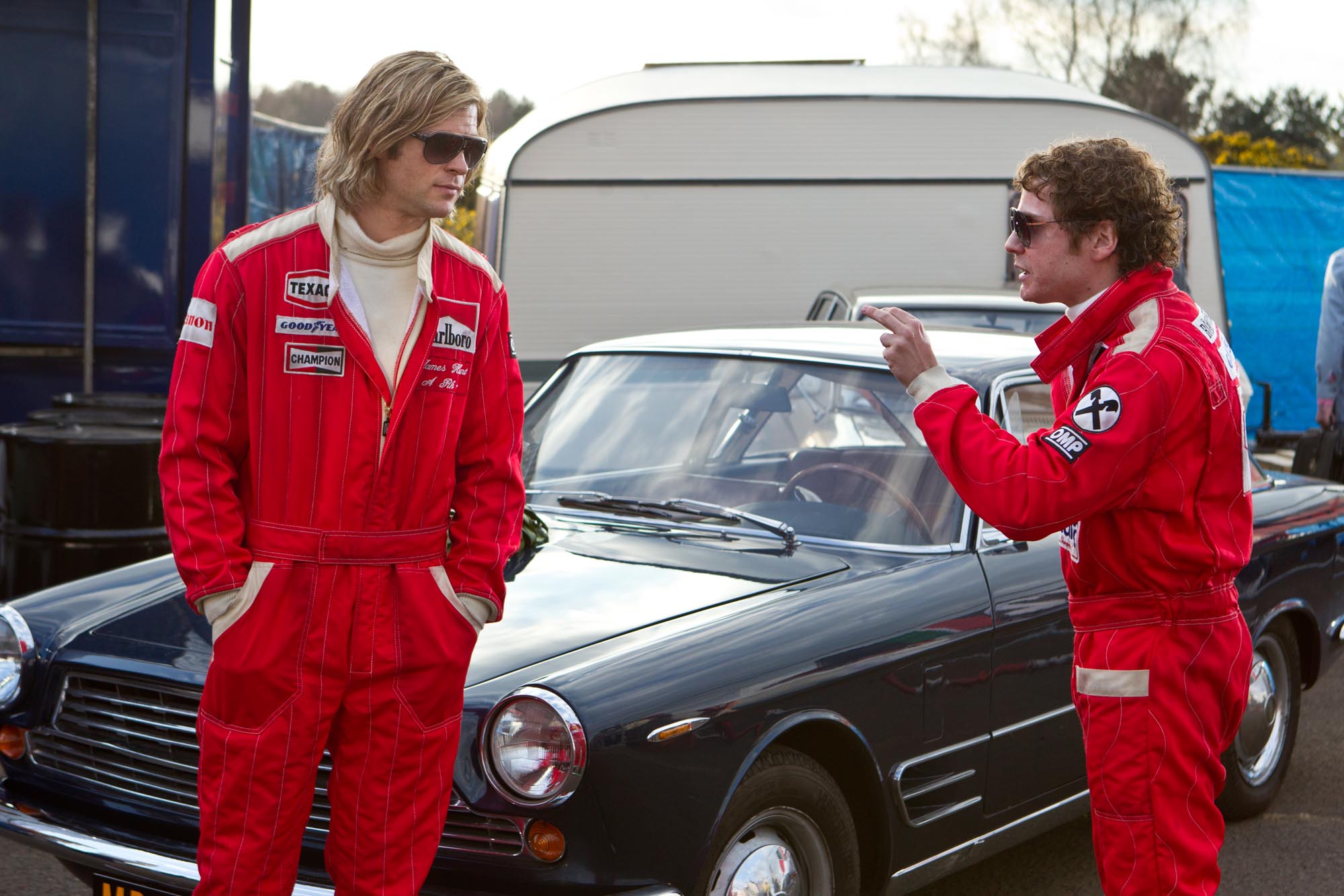 HD desktop wallpaper of two actors portraying rival racecar drivers from the movie Rush (2013), standing by a vintage car.