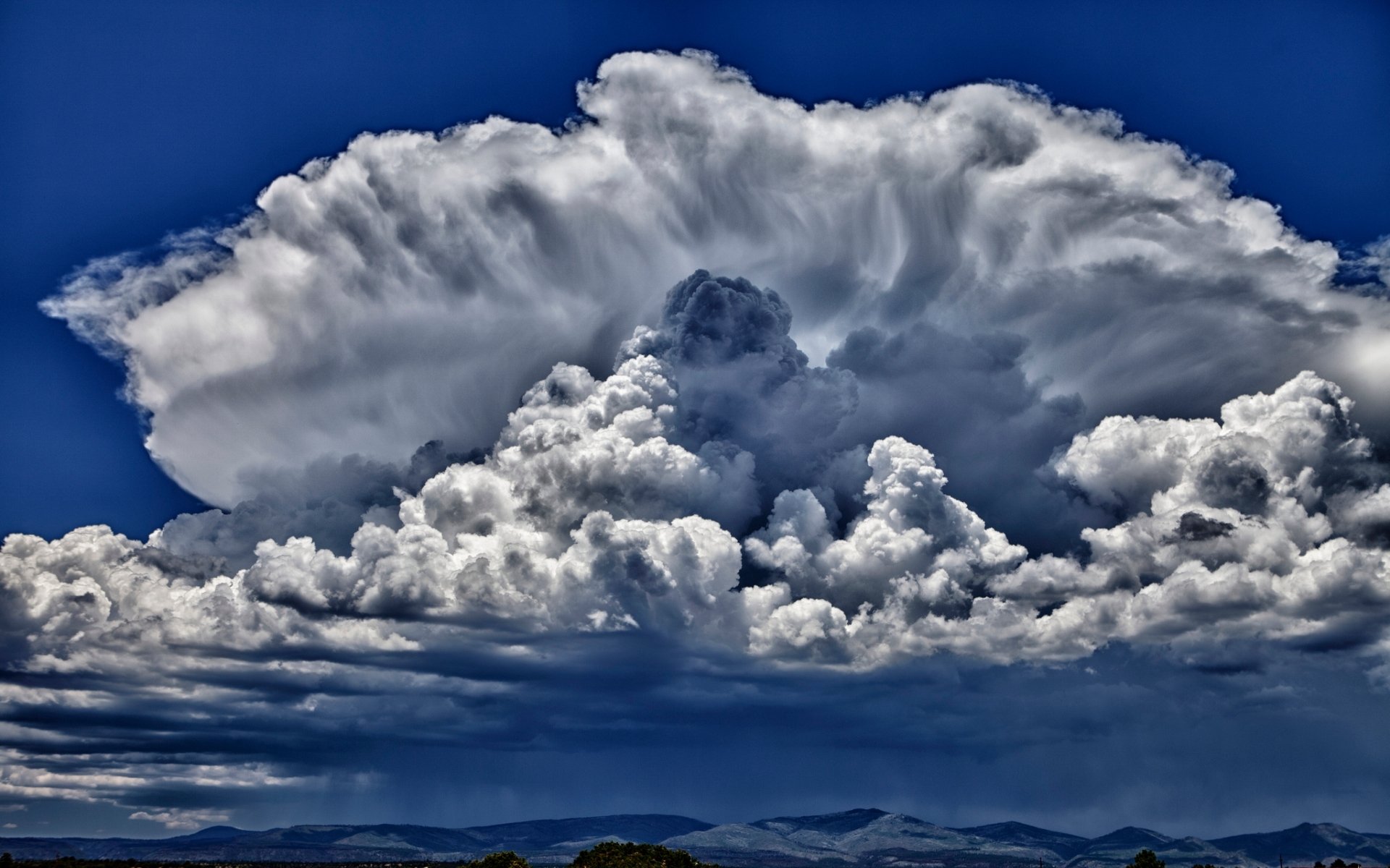 HD desktop wallpaper showing a dramatic storm cloud formation over a landscape under a deep blue sky, highlighting the power and beauty of nature.