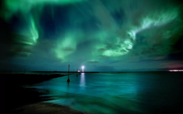 A breathtaking HD desktop wallpaper featuring the mesmerizing aurora borealis illuminating the night sky above a tranquil seaside landscape.