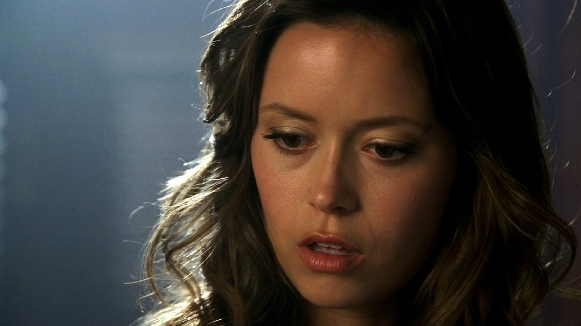 HD PC desktop wallpaper: close-up portrait of a young woman with wavy brown hair, soft studio lighting and a thoughtful expression, framed for a PC background.