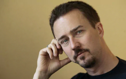 Close-up portrait of a contemplative man with short dark hair, trimmed goatee and blue-green eyes against a warm beige backdrop — 2K Quad HD PC desktop wallpaper.