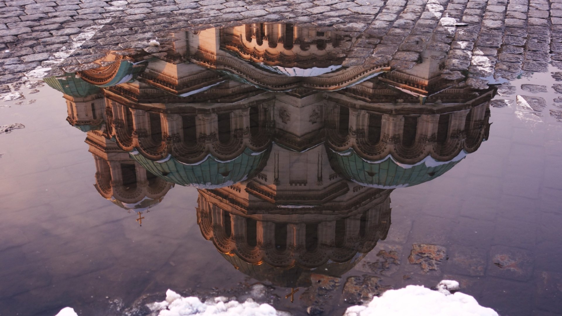 Reflection of Alexander Nevsky Cathedral, Sofia, in a cobblestone puddle with melting snow — religious landmark; 2K Quad HD PC desktop wallpaper/background.